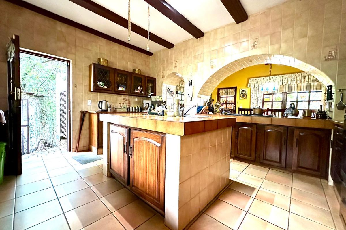 Spacious farmhouse kitchen featuring a central island, tiled countertops, exposed timber ceiling beams, and a distinctive arched architectural detail.