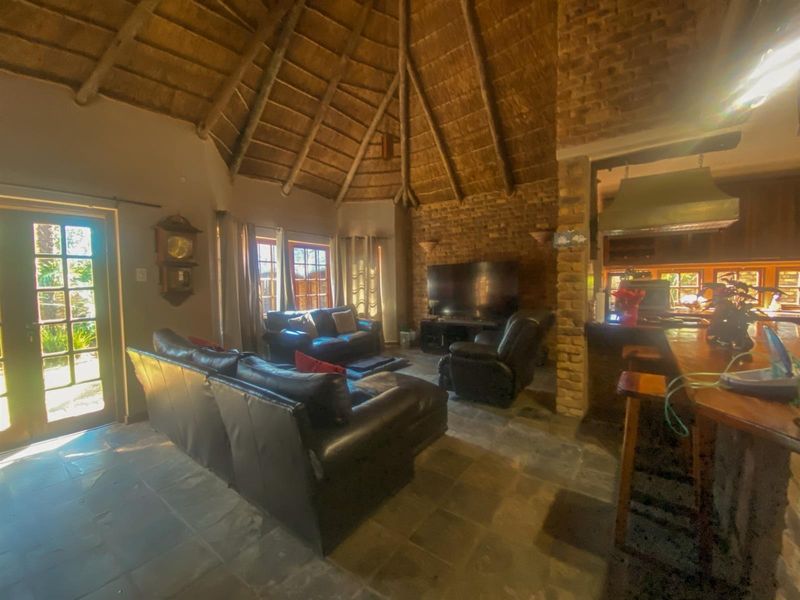 Open plan living area featuring a high thatched ceiling, exposed brickwork, stone flooring, and an integrated kitchen breakfast bar with an extractor fan.