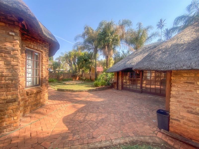 Rear courtyard featuring traditional thatched roof structures, exposed brick walls, and a circular brick paved patio area overlooking the garden.