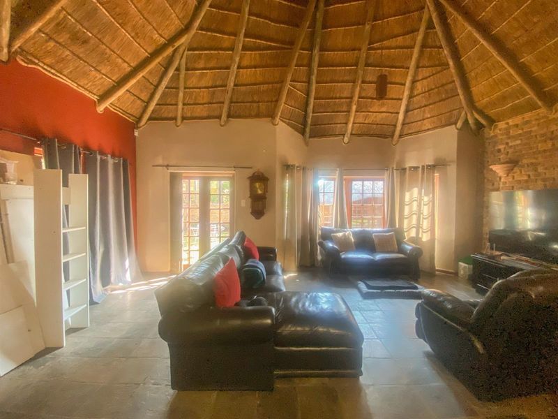 Spacious living room featuring a high exposed thatch ceiling with timber rafters, stone tile flooring, and an exposed brick feature wall.