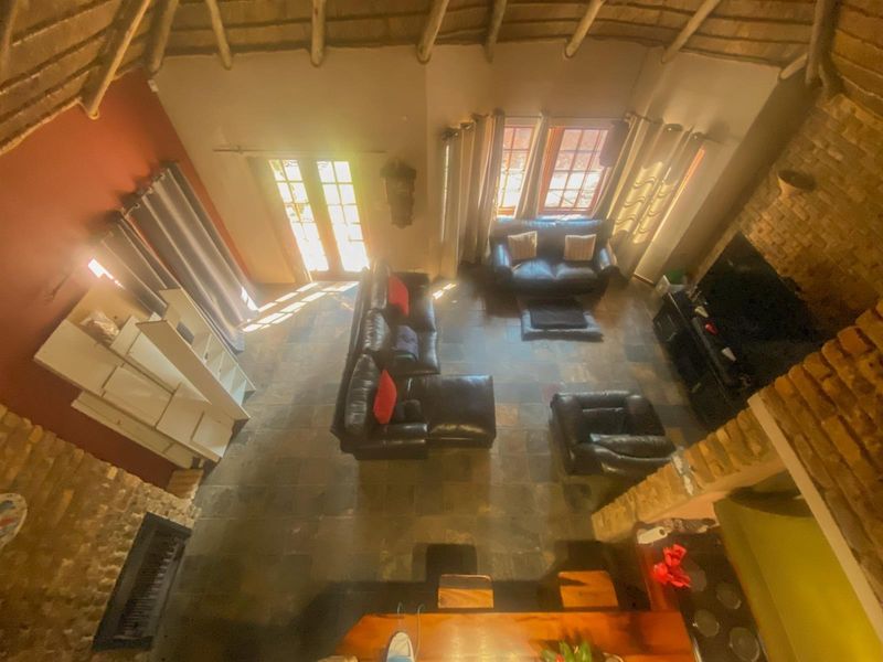 Spacious living area featuring a high thatched ceiling with exposed timber rafters, slate flooring, and a prominent stone fireplace.