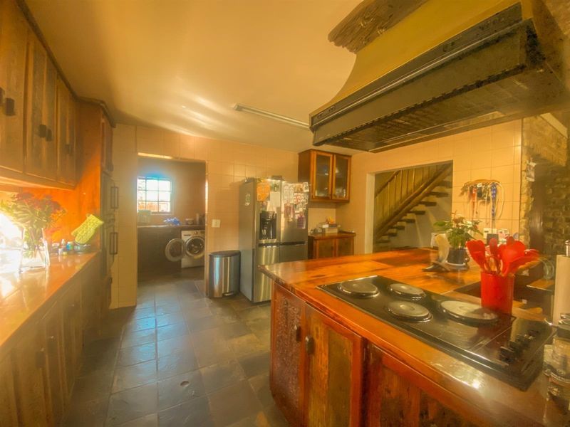 A rustic kitchen featuring wooden cabinetry, timber countertops, and a built-in electric hob, with an adjacent laundry area and staircase access.
