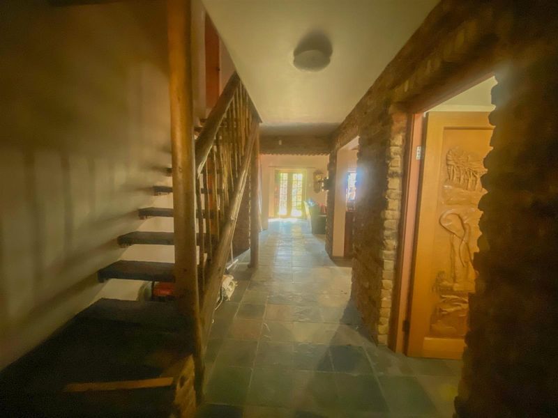 A rustic hallway featuring stone tile flooring, an exposed stone wall, and a wooden staircase leading to the upper level.