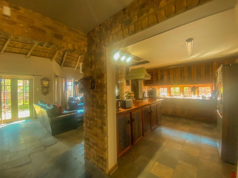 Open plan living and kitchen area featuring rustic exposed brickwork, traditional thatched ceiling, slate flooring, and warm wooden cabinetry.