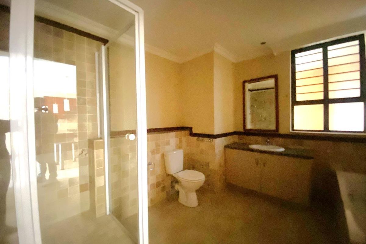 A functional bathroom featuring a glass-enclosed shower, a built-in vanity with a basin, and a toilet, finished with neutral wall tiles.