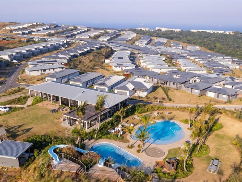 Aerial view of a residential estate featuring a communal clubhouse, swimming pools with water slides, and well-maintained landscaped grounds.