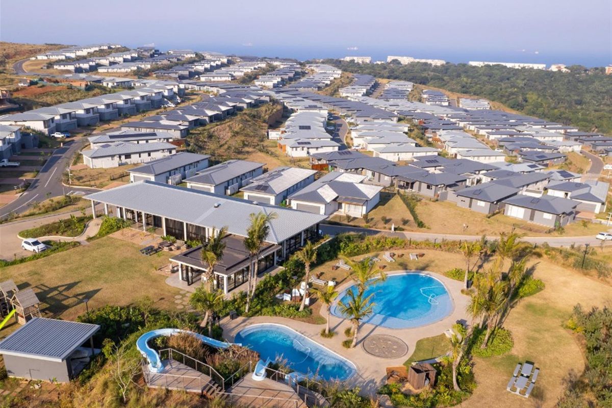 Aerial view of a residential estate featuring a communal clubhouse, swimming pools with water slides, and well-maintained landscaped grounds.