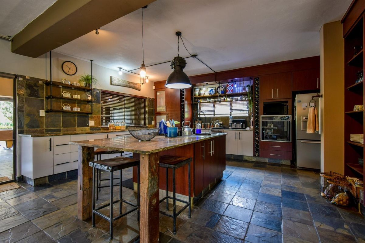 Spacious kitchen featuring a large central island, built-in oven, integrated microwave, and extensive cabinetry with slate-style tile flooring and industrial-style lighting.