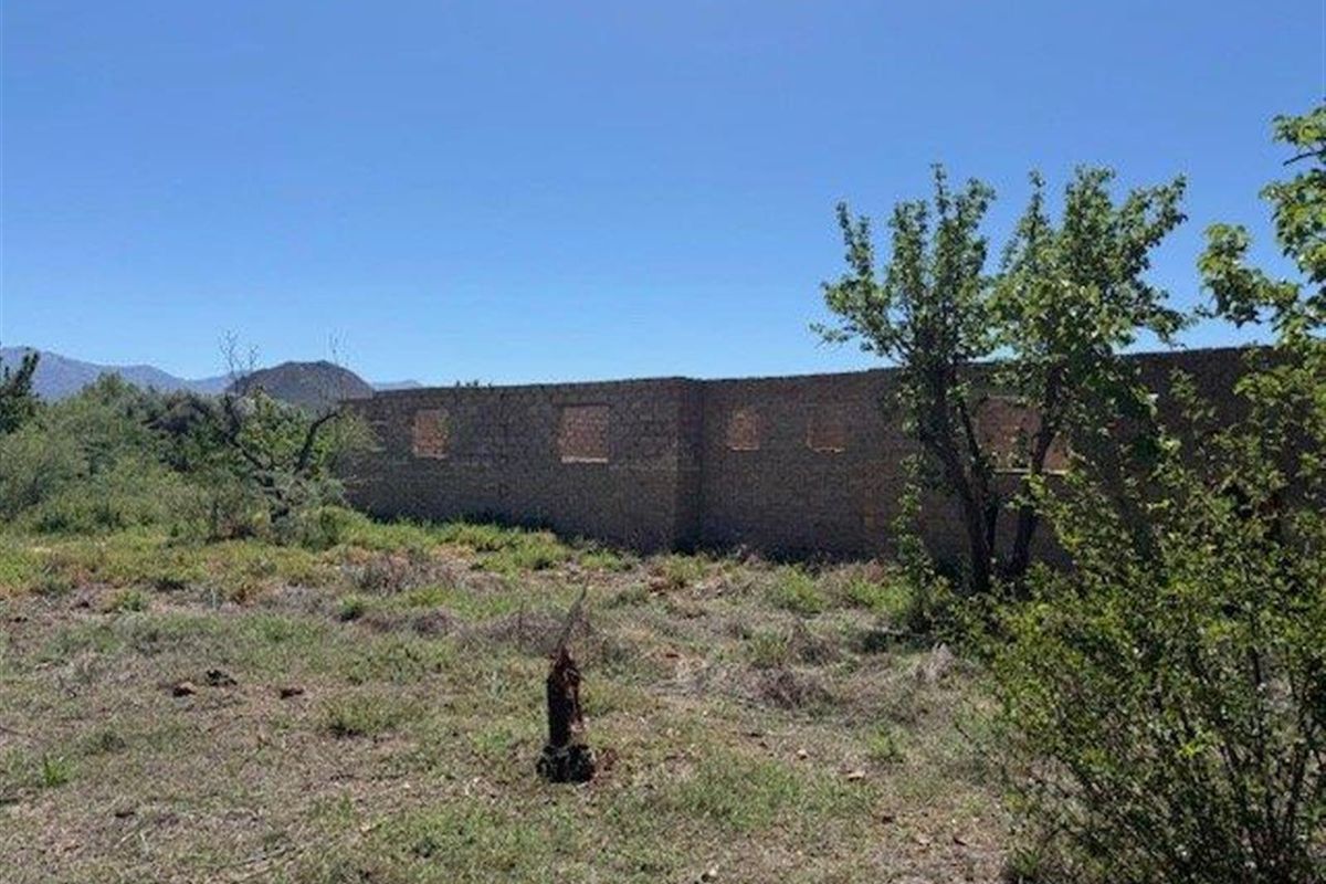 An unfinished masonry structure set within a large, overgrown plot of land, offering significant potential for development or renovation.
