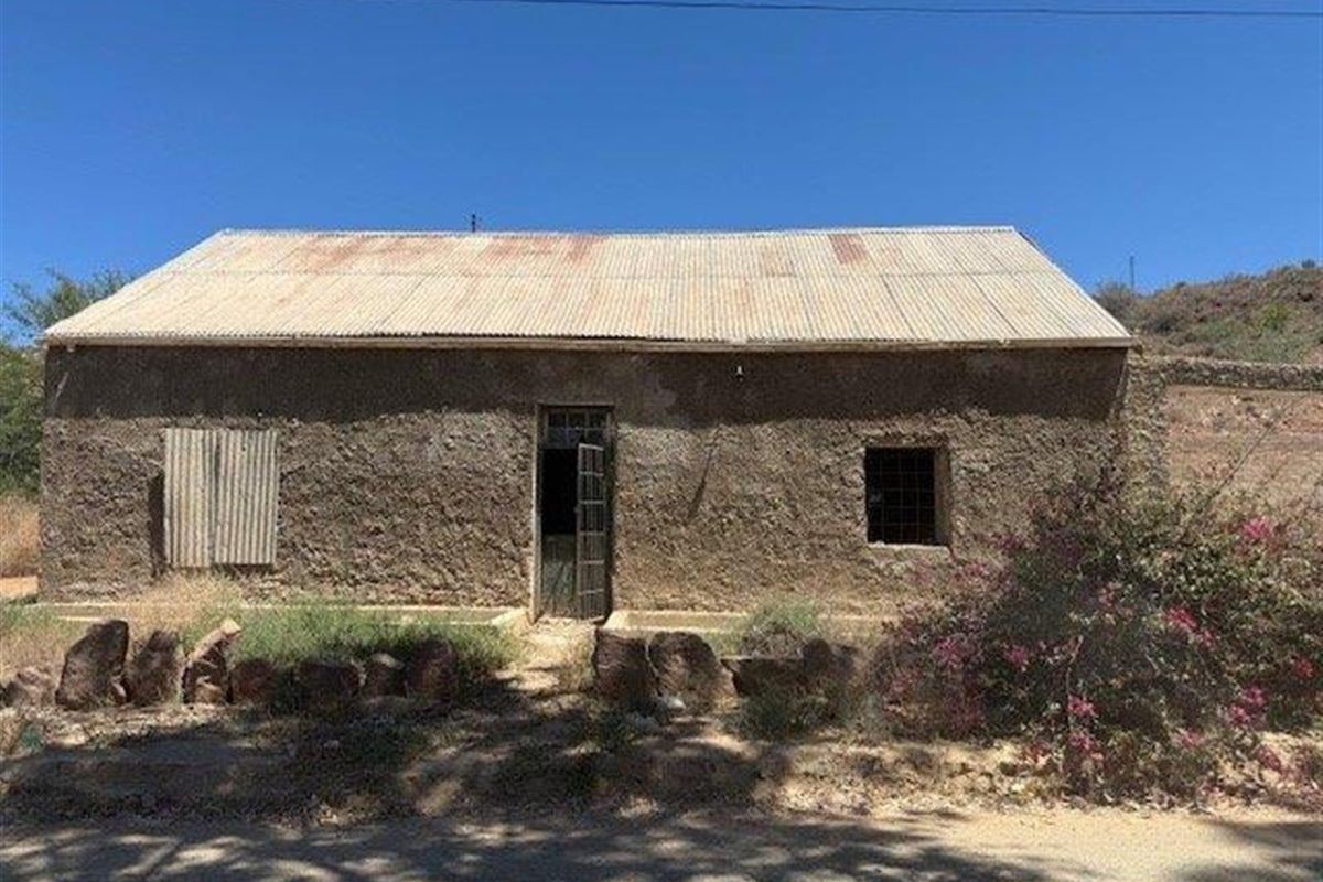 A rustic, single-story dwelling featuring a corrugated metal roof and weathered exterior walls, presenting a significant renovation opportunity in a rural setting.