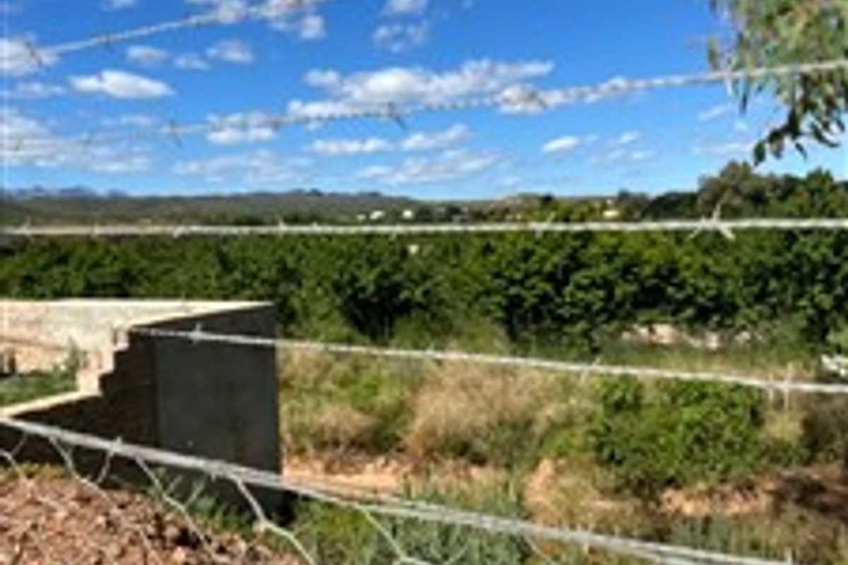 A view of the surrounding landscape and vegetation from the vacant residential property, featuring a perimeter fence and partial retaining wall.