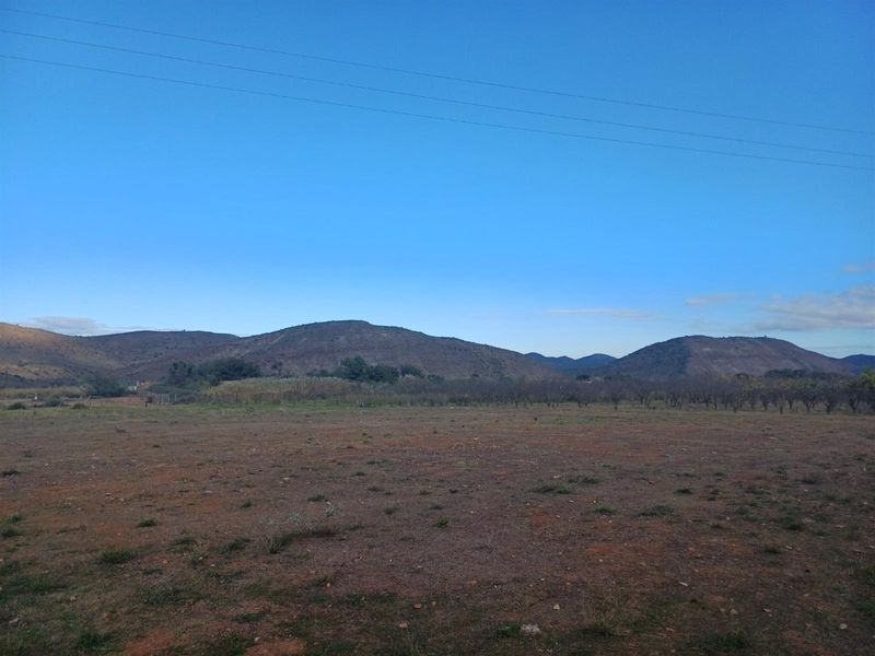 A wide-angle view of a vacant residential plot featuring natural terrain and scenic mountain vistas in the background.