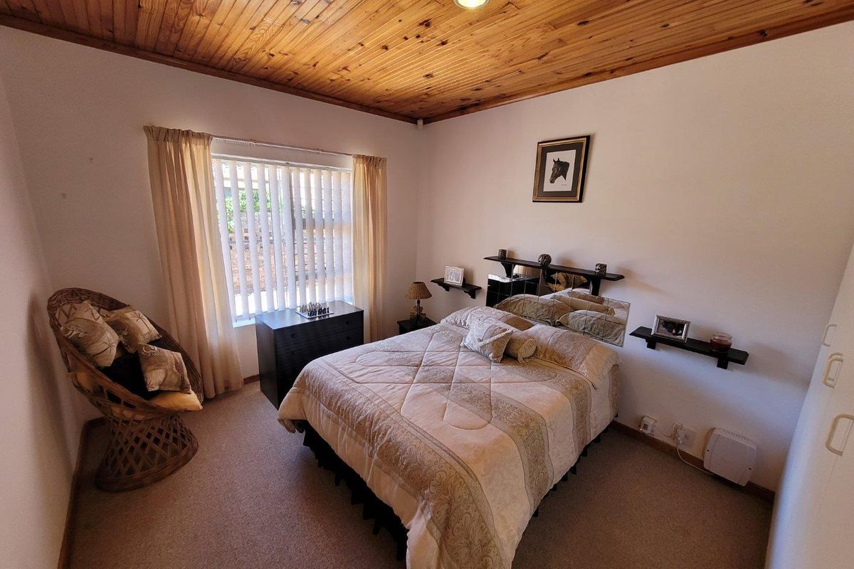A cozy bedroom featuring a warm timber tongue and groove ceiling, neutral carpeting, and a built-in wardrobe with natural light from the window.