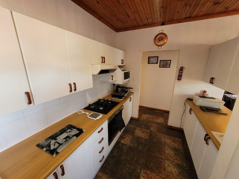 A functional kitchen featuring white cabinetry, timber ceiling, gas hob, built-in oven, and tiled flooring.