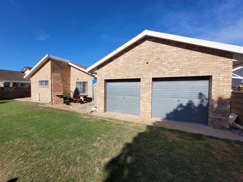 Rear view of the property featuring a double garage with roller doors, a brick facade, and a built-in outdoor braai area.