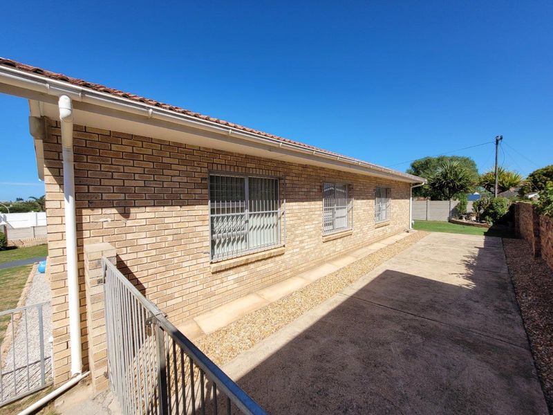 Rear exterior view of the house featuring face brick walls, security bars on windows, concrete paving, and a tiled roof.