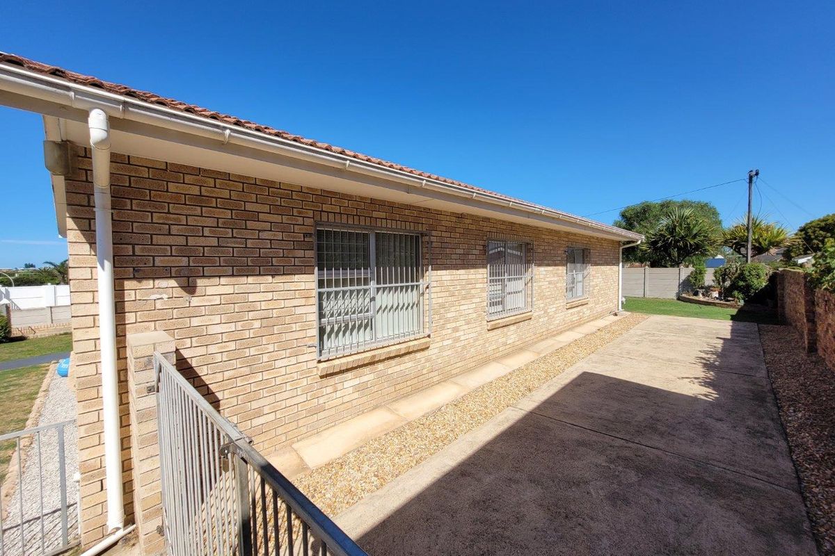 Rear exterior view of the house featuring face brick walls, security bars on windows, concrete paving, and a tiled roof.