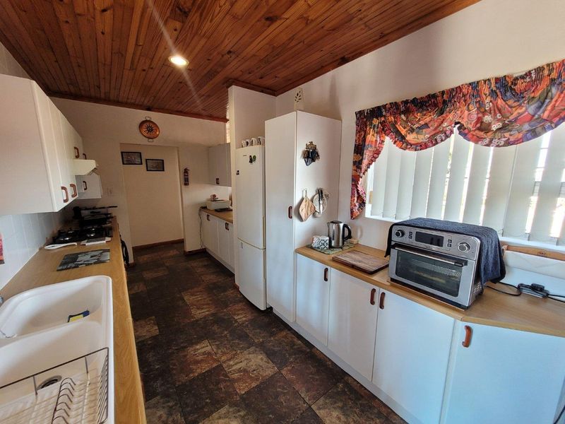 A functional kitchen featuring timber ceilings, white cabinetry, laminate countertops, and a double basin sink, offering a dated but practical layout.
