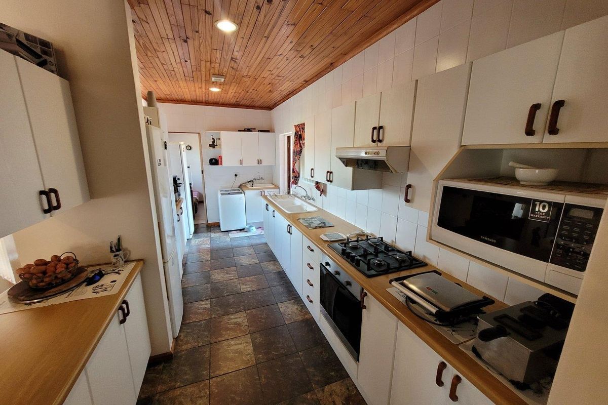 A functional galley-style kitchen featuring white cabinetry, a gas hob, built-in oven, and a distinctive timber-clad ceiling with tiled flooring.