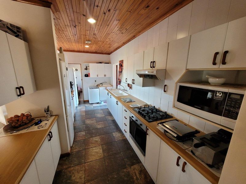 A functional galley-style kitchen featuring white cabinetry, a gas hob, built-in oven, and a distinctive timber-clad ceiling with tiled flooring.