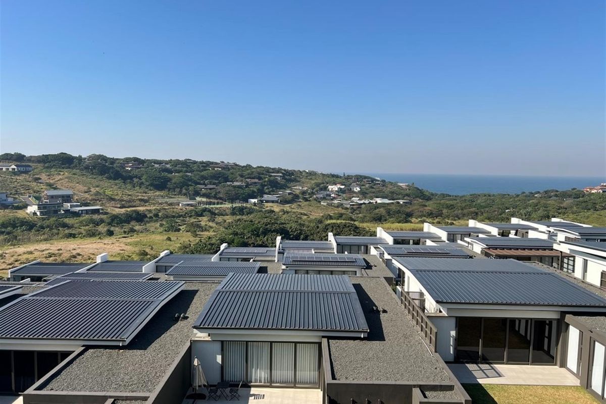 An elevated aerial view of a modern residential complex featuring metal roofs with integrated solar panels and scenic coastal landscape views.