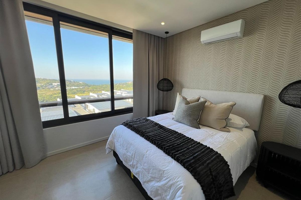 A modern, well-maintained bedroom featuring a large window with scenic views, split-system air conditioning, and stylish textured wallpaper.