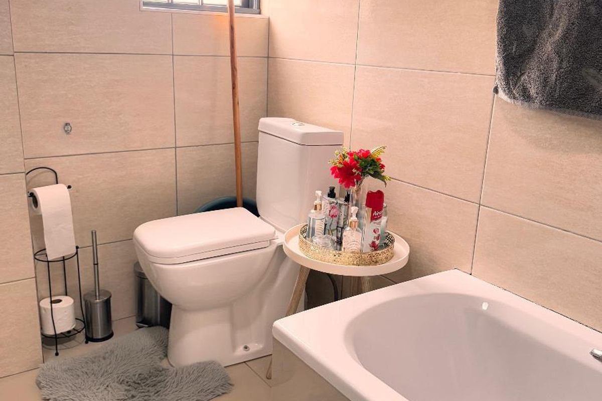 A well-maintained bathroom featuring neutral wall tiles, a built-in bathtub, and a modern toilet with security bars on the window.