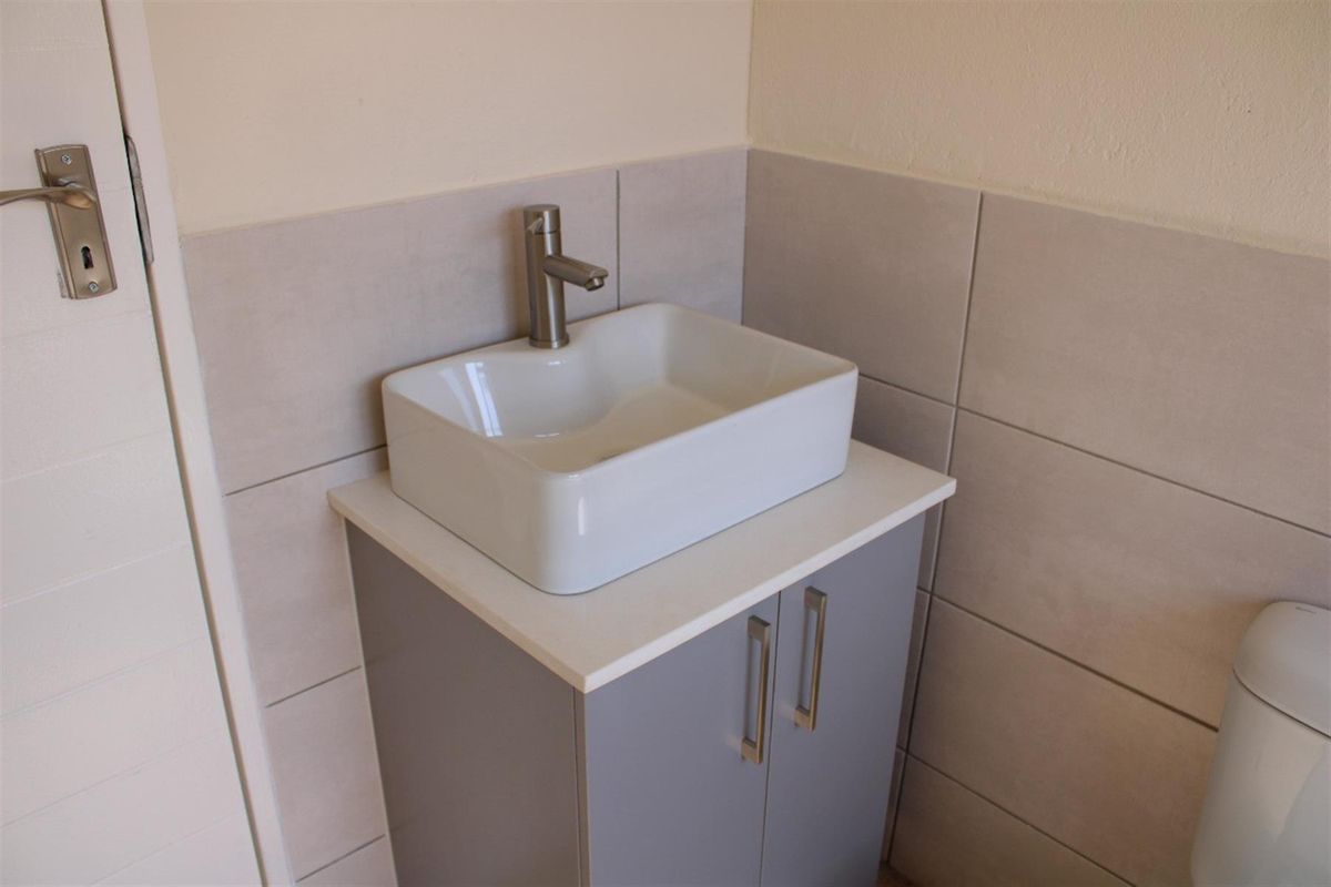 A compact bathroom featuring a modern vessel sink, vanity cabinet, and neutral wall tiling.