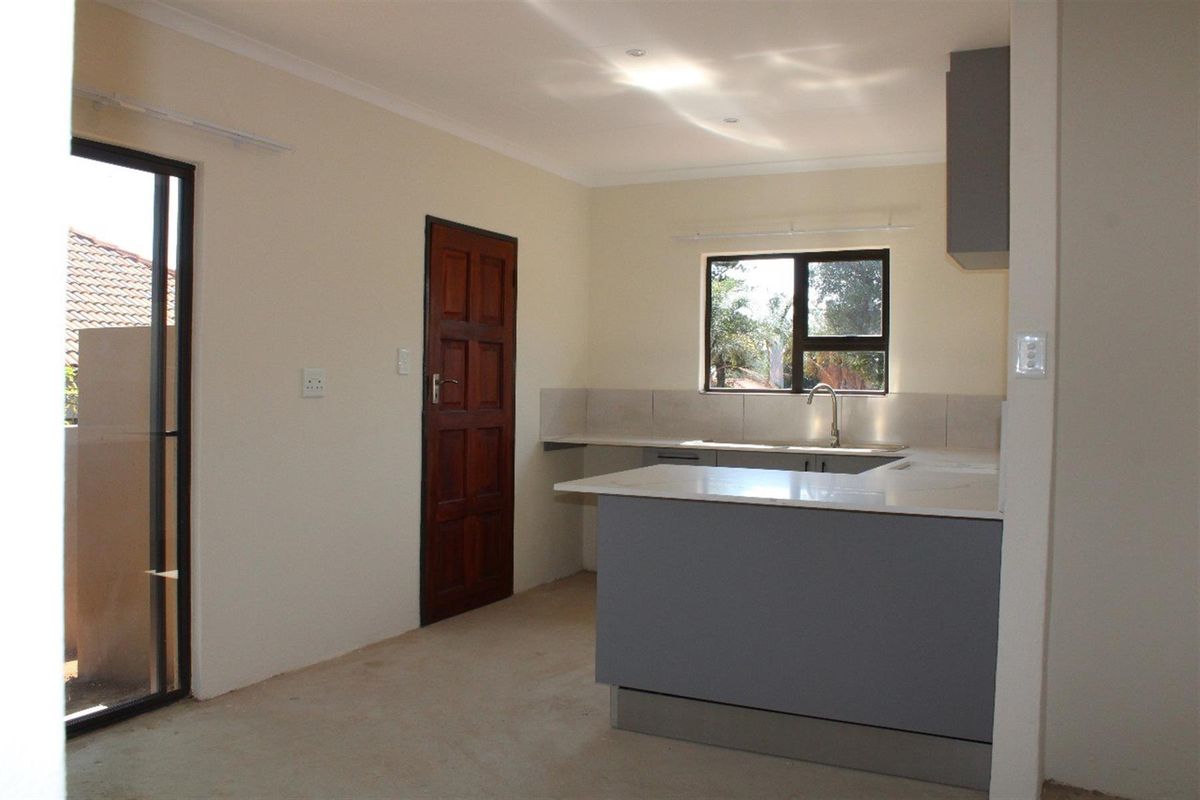 A functional kitchen area featuring modern grey cabinetry, stone-look countertops, a stainless steel sink, and direct access to an outdoor patio area.