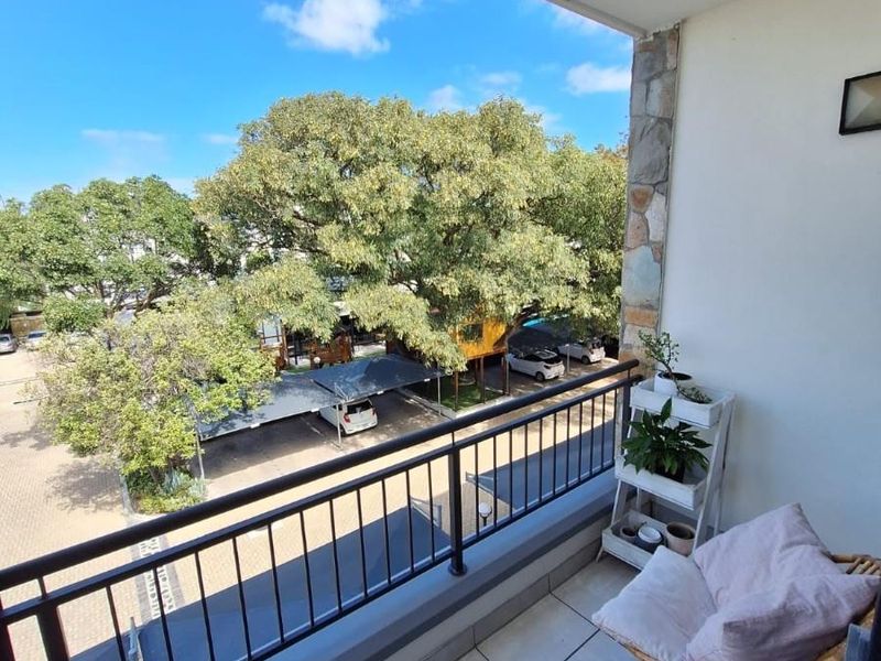 A well-maintained balcony featuring tiled flooring, a metal balustrade, and a decorative stone-clad wall, offering an elevated view of the complex parking area.