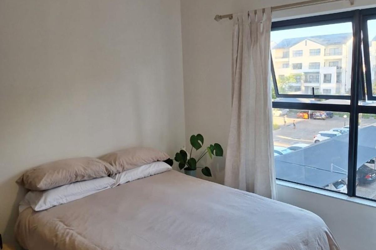 A well-lit bedroom featuring tiled flooring, a modern pendant light, and a large window with views of the apartment complex parking area.