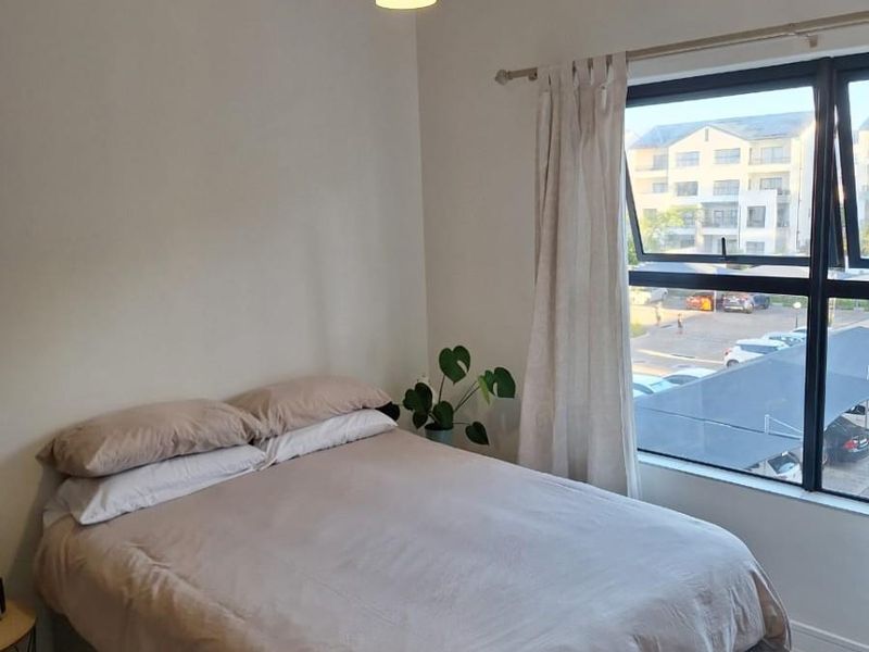 A well-lit bedroom featuring tiled flooring, a modern pendant light, and a large window with views of the apartment complex parking area.