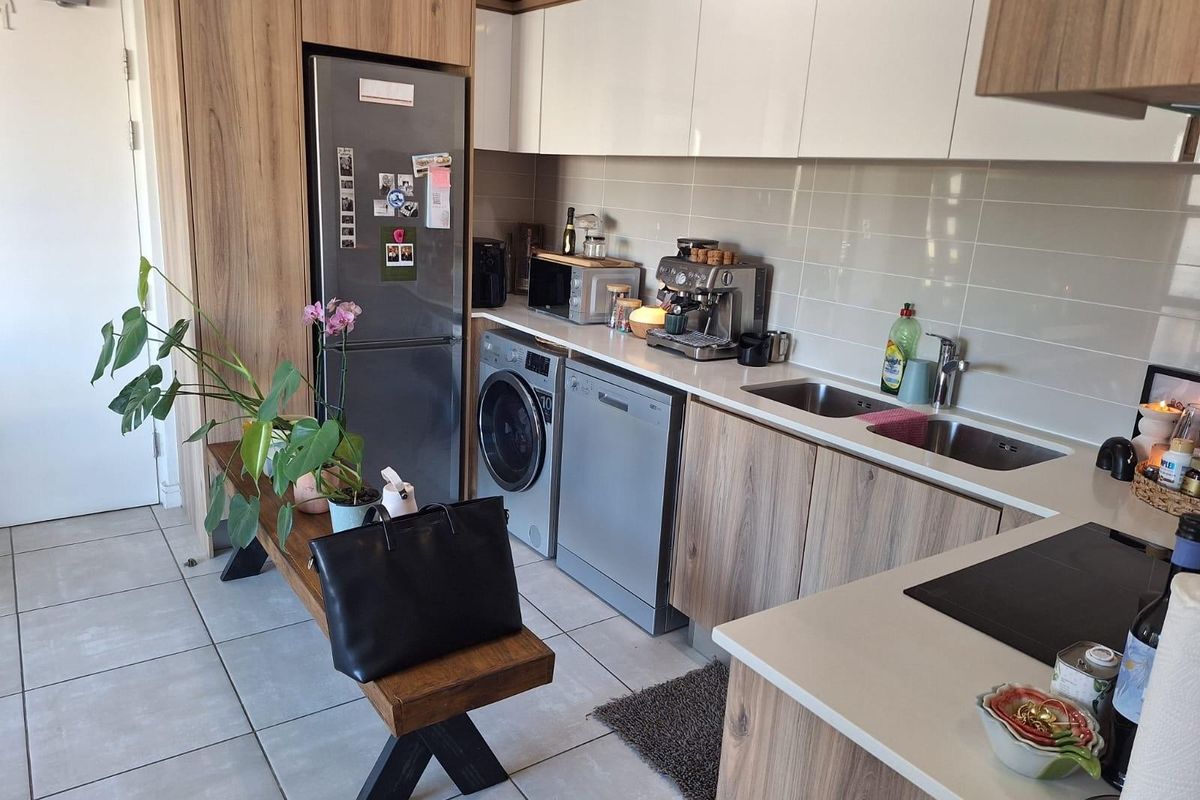 Modern kitchen featuring wood-grain cabinetry, stone countertops, integrated appliances, and a double bowl sink with a tiled splashback.
