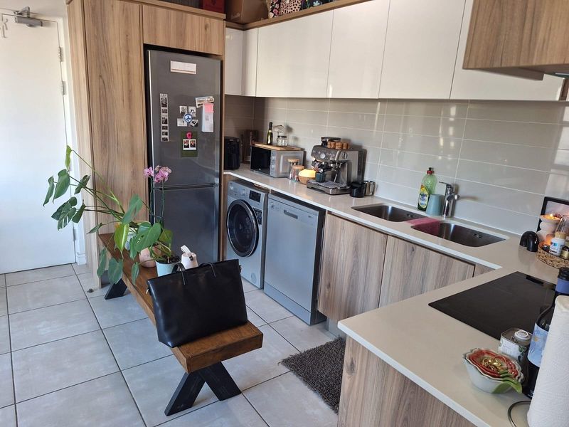 Modern kitchen featuring wood-grain cabinetry, stone countertops, integrated appliances, and a double bowl sink with a tiled splashback.