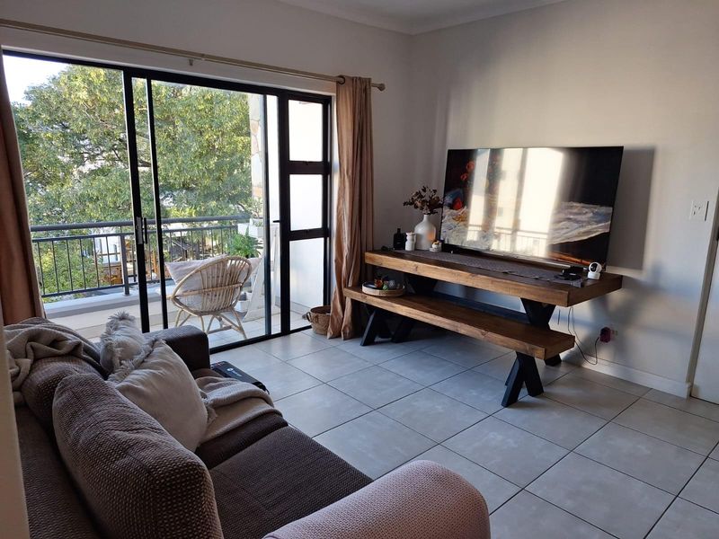 A bright living room featuring large sliding glass doors that open onto a balcony, with neutral ceramic floor tiles throughout.