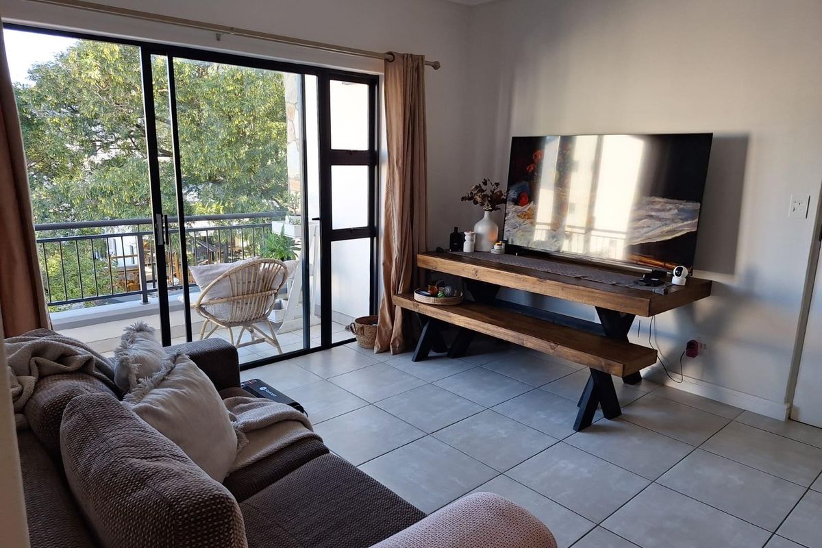 A bright living room featuring large sliding glass doors that open onto a balcony, with neutral ceramic floor tiles throughout.