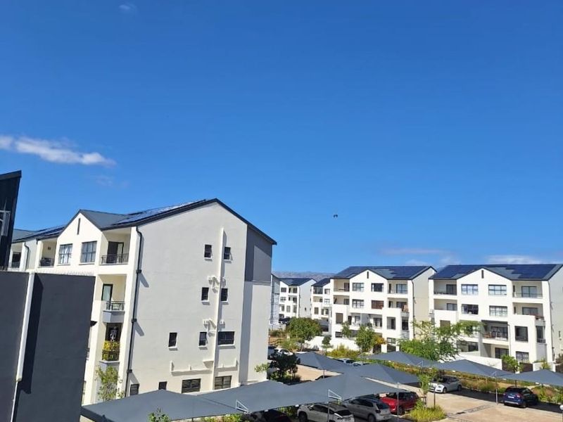 An elevated view of a modern apartment complex featuring paved parking areas with shade cloth carports and multi-story residential buildings with solar panels.
