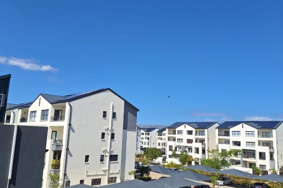 An elevated view of a modern apartment complex featuring paved parking areas with shade cloth carports and multi-story residential buildings with solar panels.