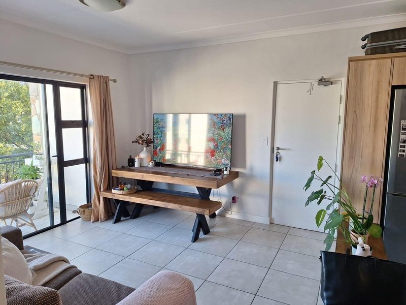 A bright living room featuring tiled flooring, a sliding glass door leading to a balcony, and built-in cabinetry.