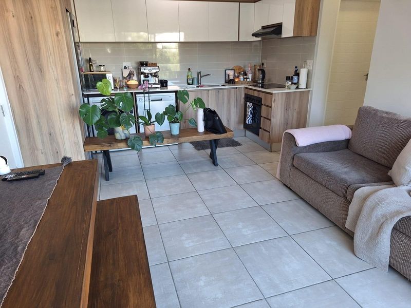 Modern open-plan living area featuring a contemporary kitchen with wood-grain cabinetry, integrated appliances, and neutral tiled flooring throughout.