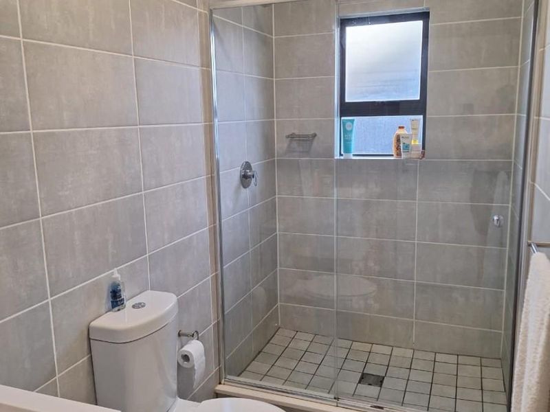 Modern bathroom featuring a glass-enclosed shower, tiled walls, a white vanity basin, and a standard toilet.