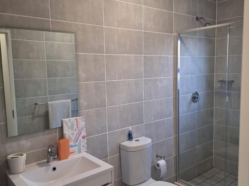 Modern bathroom featuring grey wall tiles, a white vanity cabinet with integrated basin, a toilet, and a glass-enclosed shower.