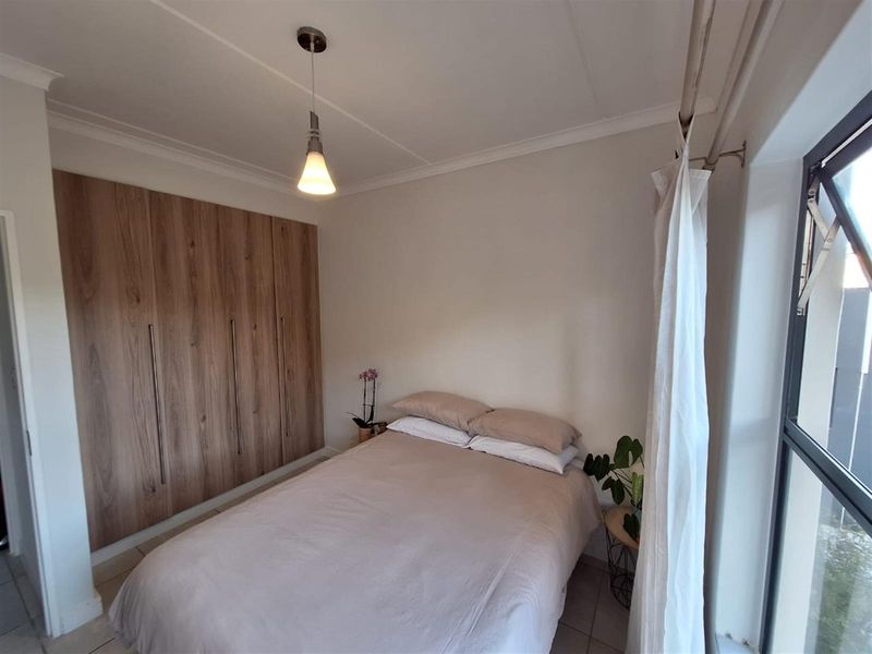 A well-maintained bedroom featuring modern wood-finish built-in cupboards, tiled flooring, and a large window allowing for natural light.