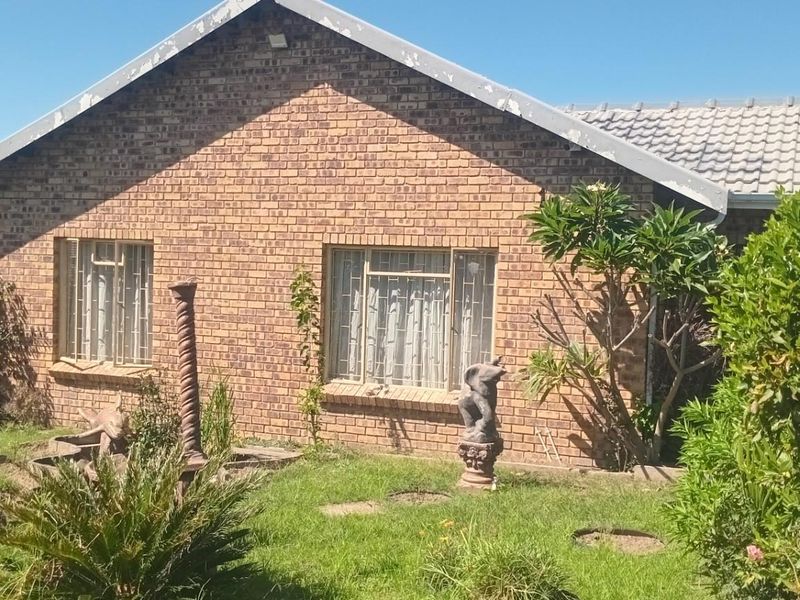 A view of the rear brick facade of the house, featuring a garden area and established landscaping.