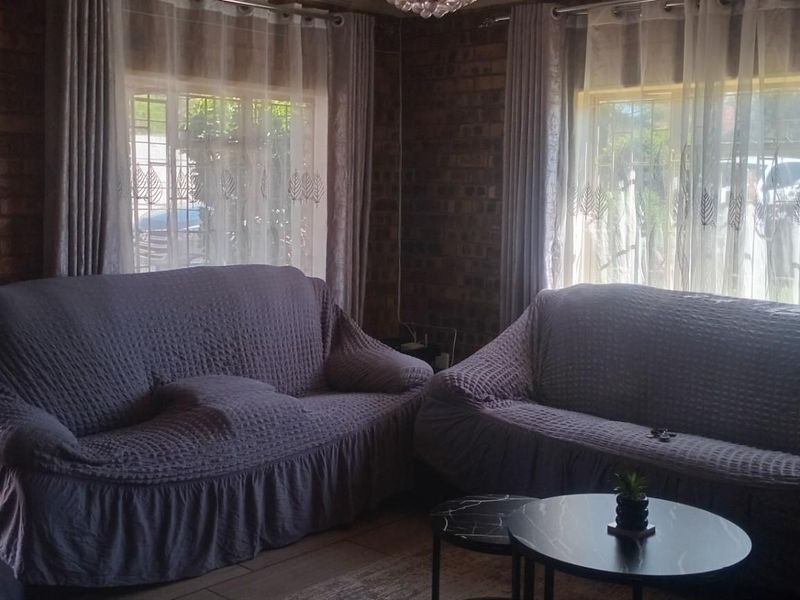 A living room featuring exposed brick walls, tiled flooring, and large windows with security bars, providing a rustic and secure living space.