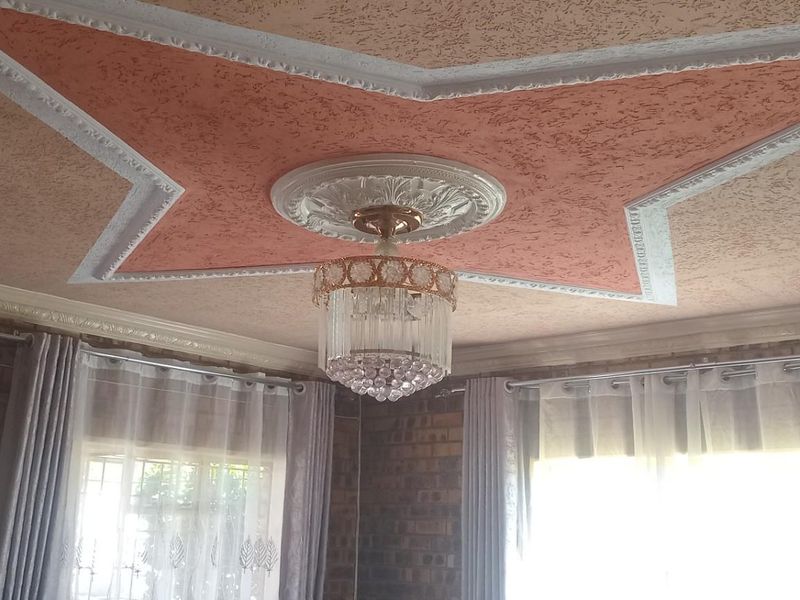 Living area featuring a decorative star-shaped ceiling molding with a central crystal chandelier and exposed brick wall finishes.
