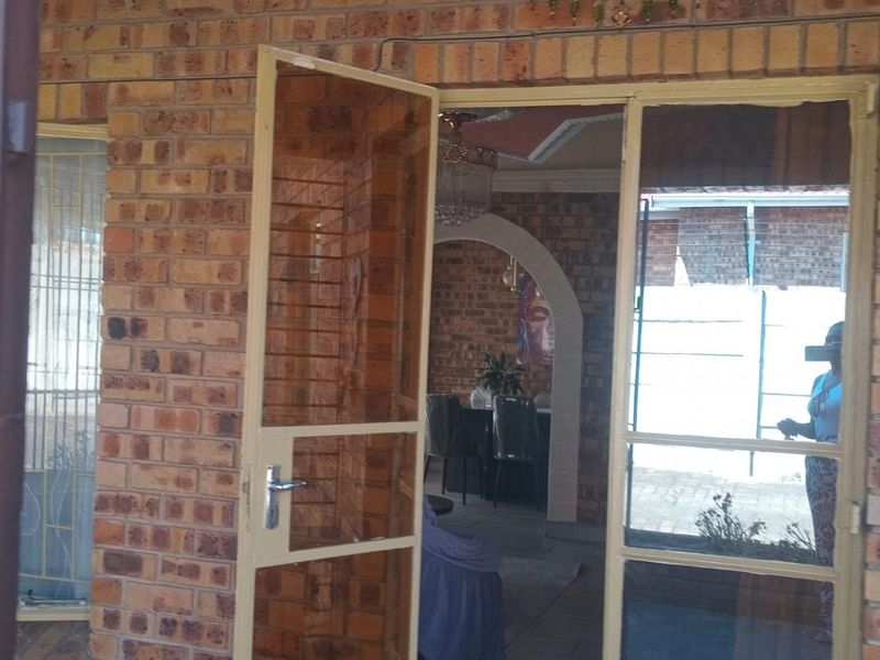 View of the home entrance featuring a face-brick facade, security screen door, and a glimpse into the interior living space.