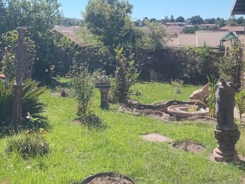 A private rear garden featuring a lawn, established greenery, and a small decorative water feature adjacent to the brick exterior of the house.