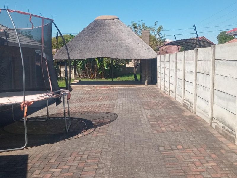 Spacious paved rear courtyard featuring a thatched lapa structure, enclosed by high precast concrete perimeter walling with electric fencing.