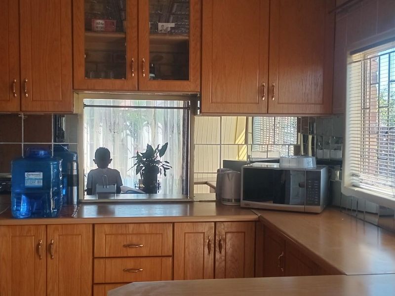 A traditional kitchen featuring wood-finish cabinetry, built-in oven, and a window with security bars, offering a functional layout with ample storage space.